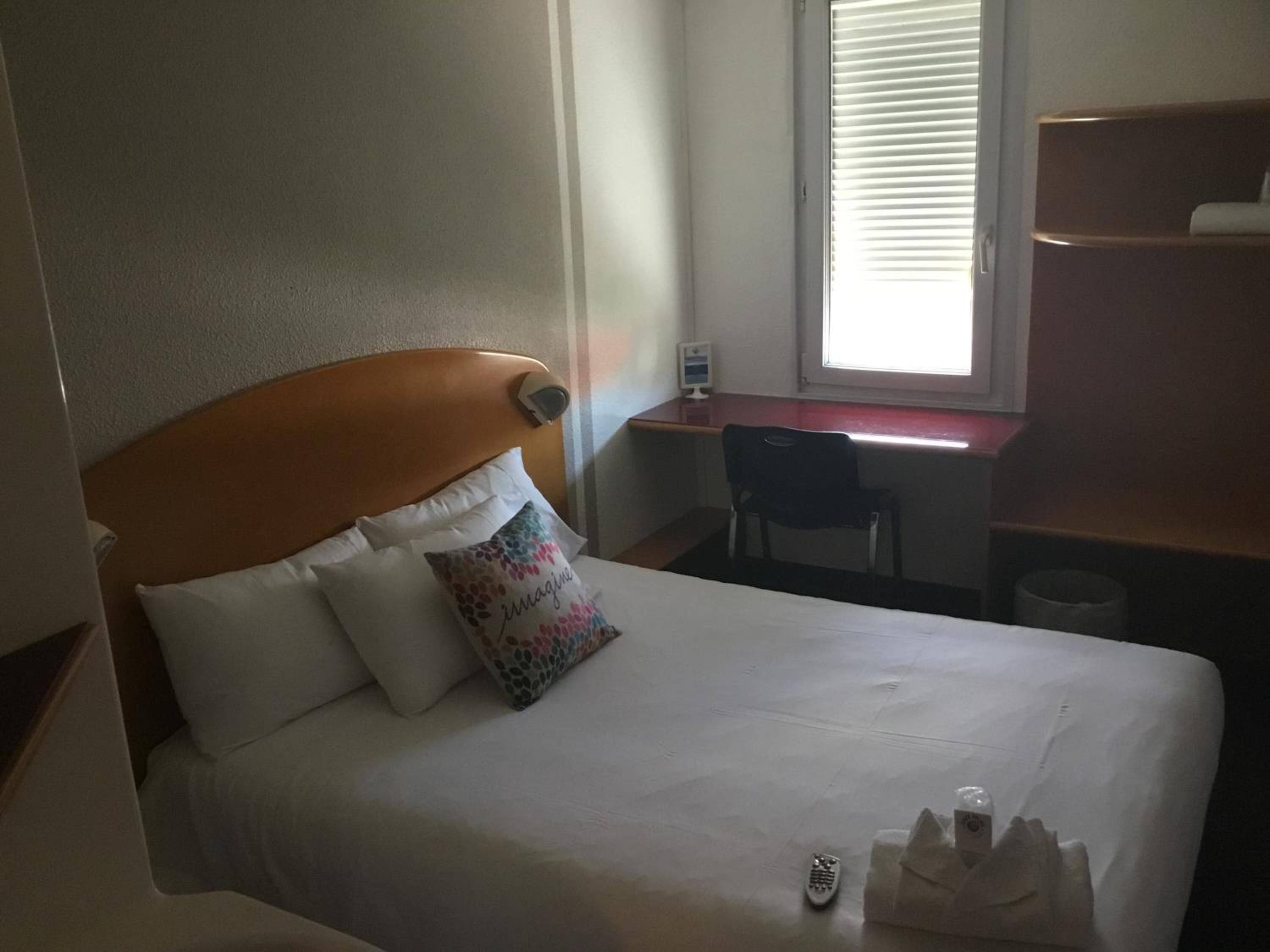 A hotel room with a bed, a desk, a chair, and a window with blinds.