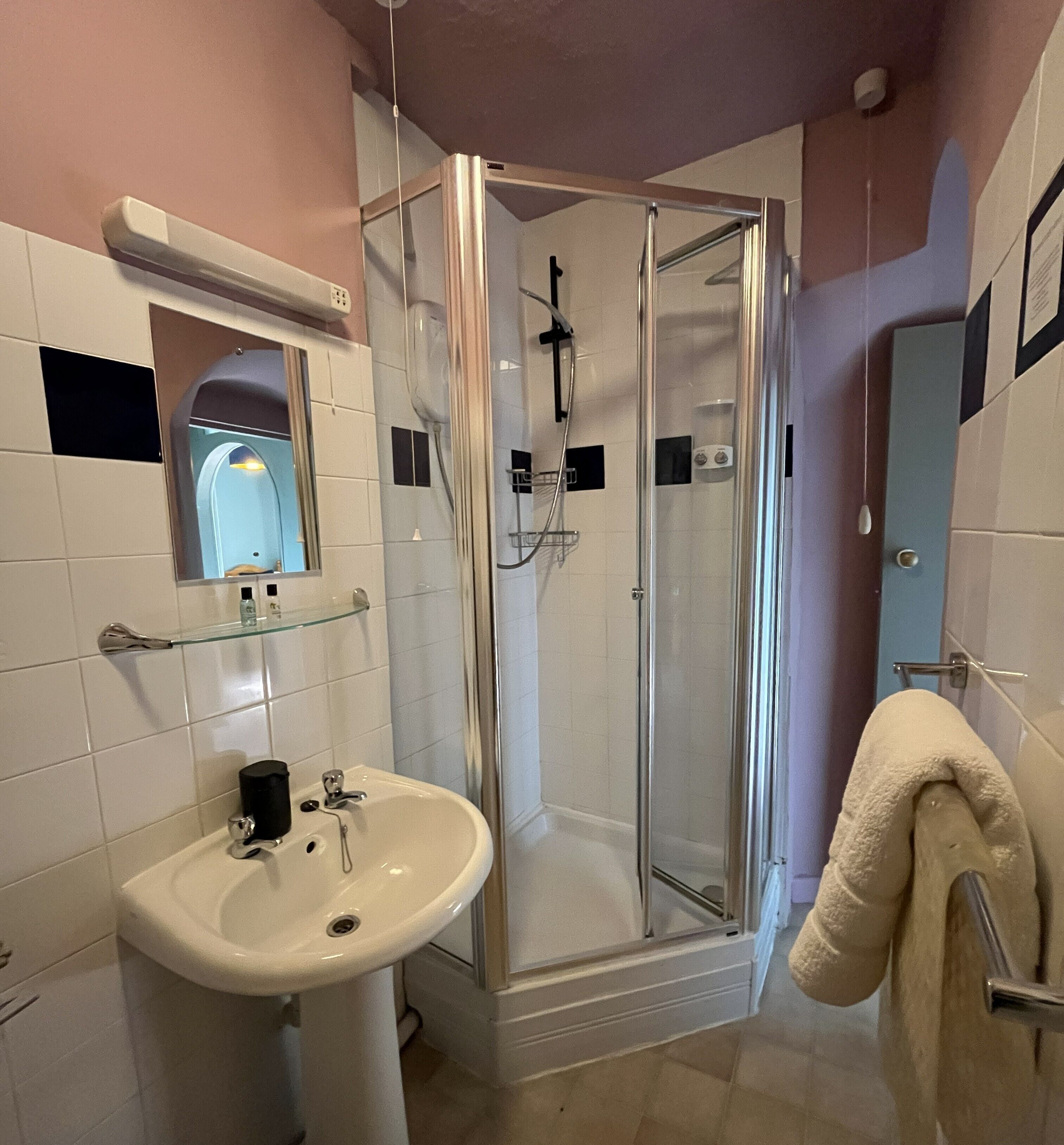 A bathroom with a glass-enclosed shower, a sink with a mirror above it, and a towel rack.