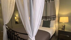 Un letto a baldacchino con un testiera, un comodino con una lampada e un tavolino da notte.