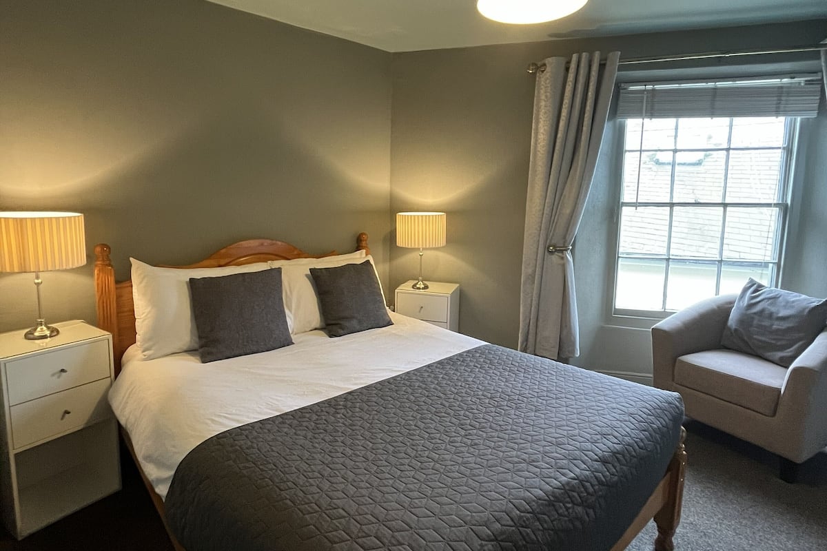 A neatly arranged hotel room with a large bed, bedside lamps, a chair, and a window with curtains.