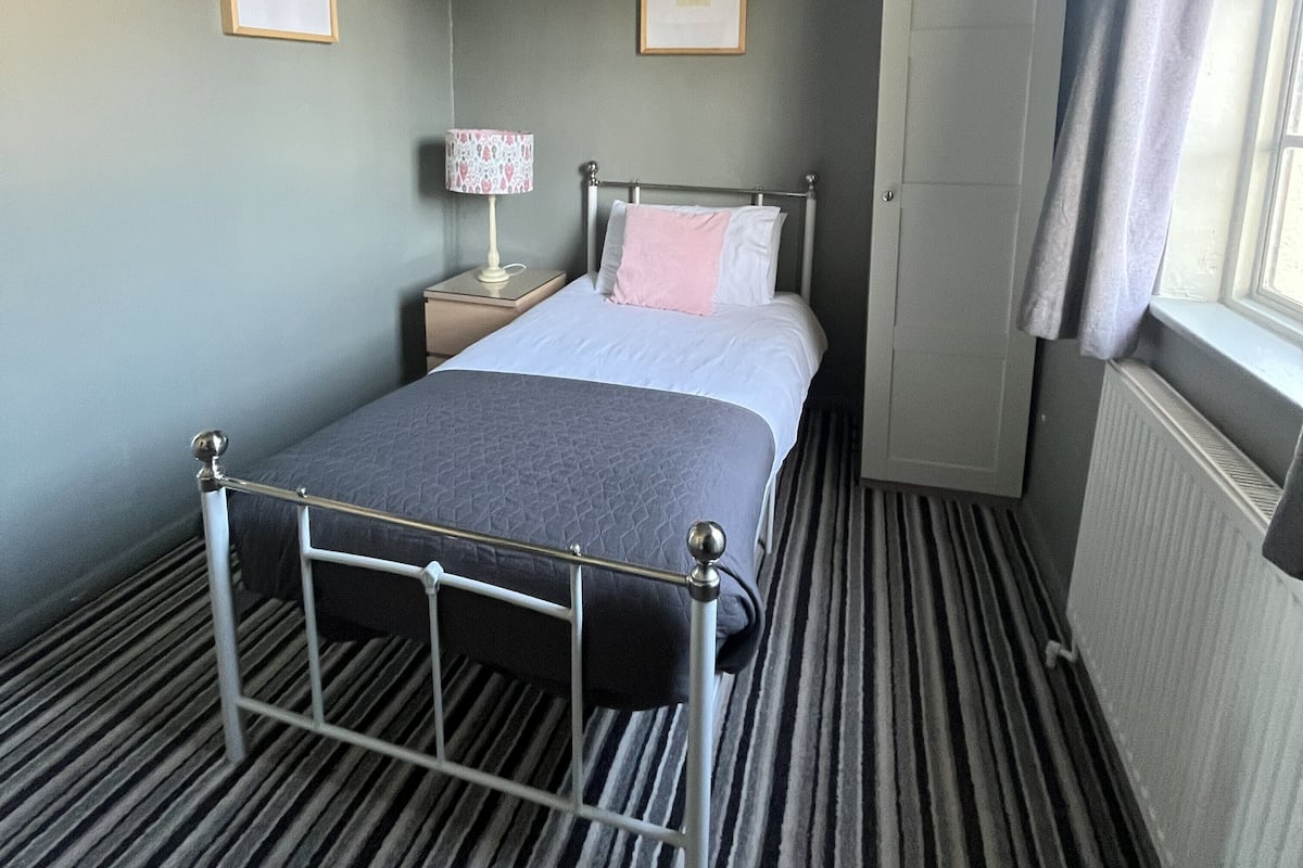 A single bed with a metal frame, a bedside table with a lamp, a door, and a radiator.