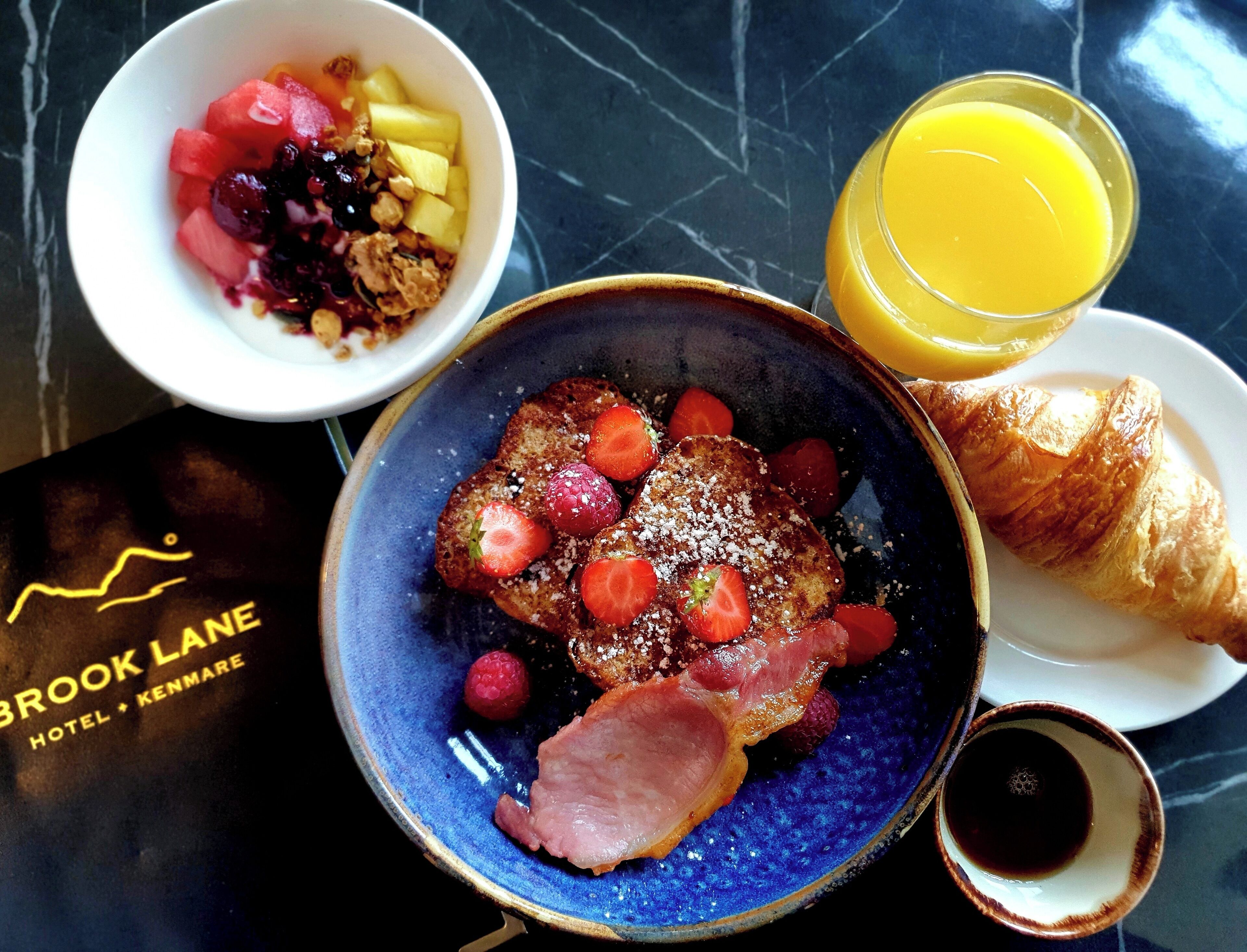 A breakfast setting with toast, strawberries, ham, a croissant, and a glass of orange juice on a marble table.