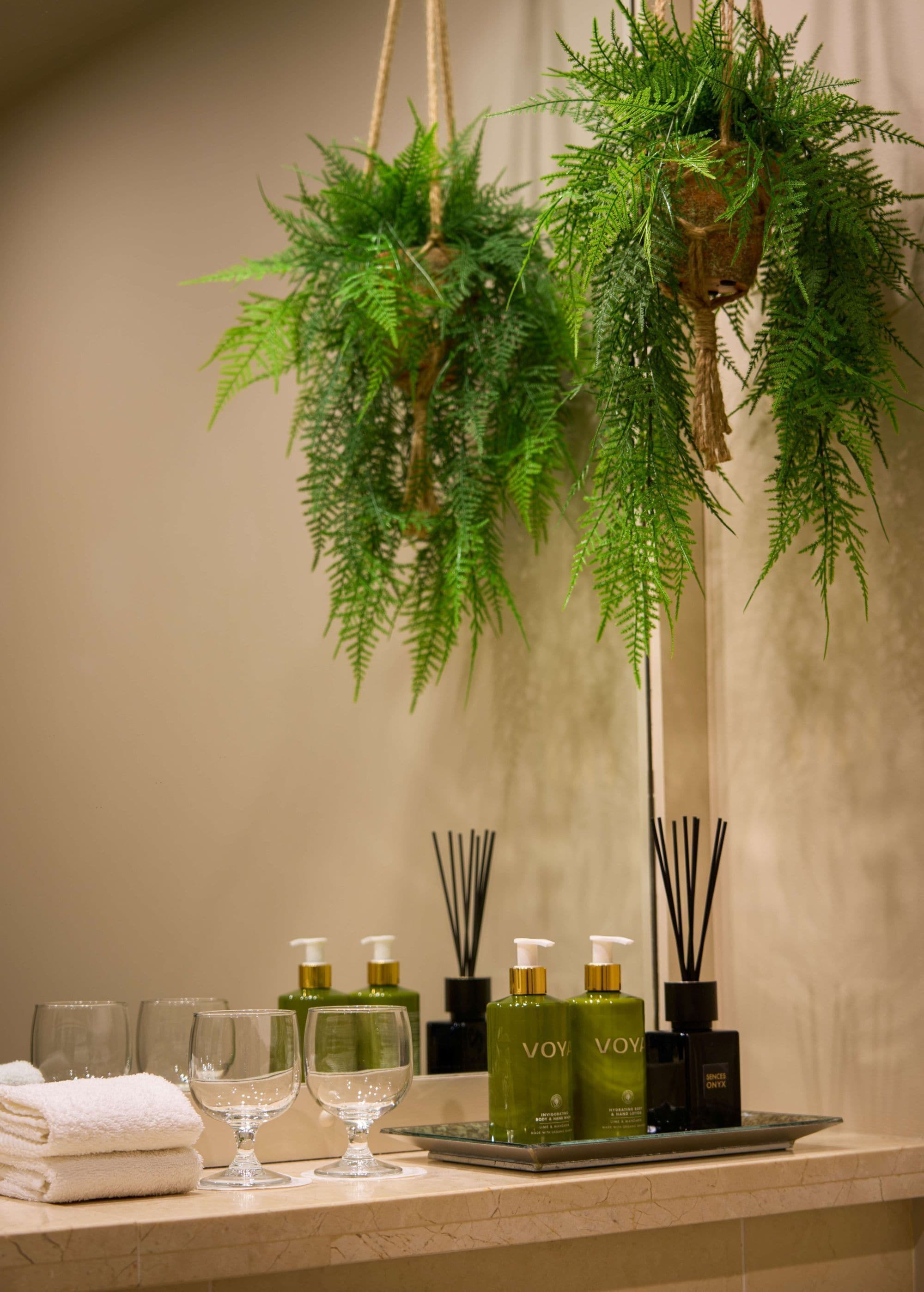 A bathroom counter with a hanging plant, a tray with bottles, and a stack of towels.
