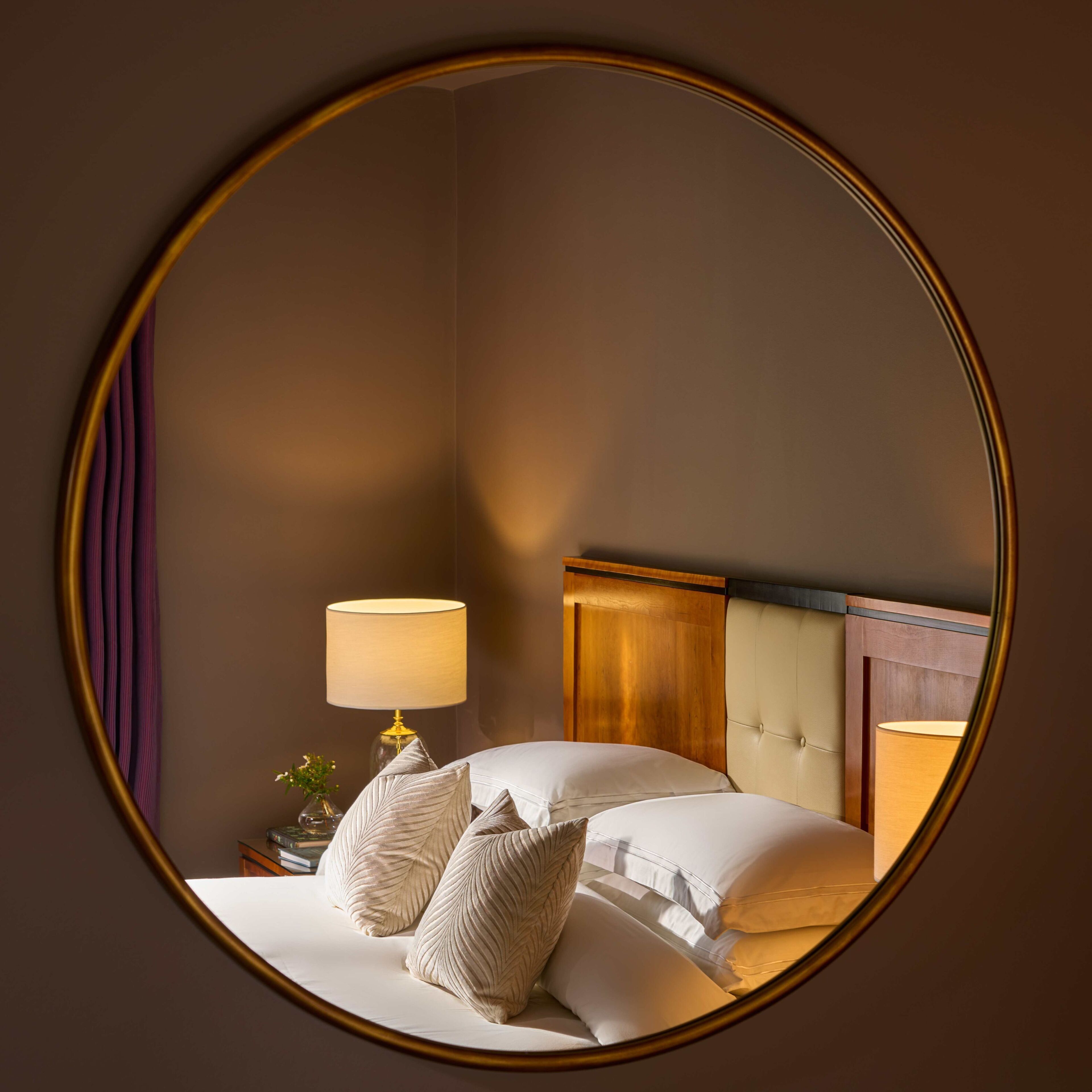 A hotel room with a bed, a bedside lamp, and a mirror.