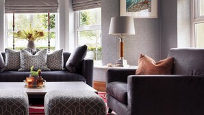 A modern living room with a sofa, armchair, and ottoman, a table with a candle, and a lamp. - Brook Lane Hotel (Kenmare)