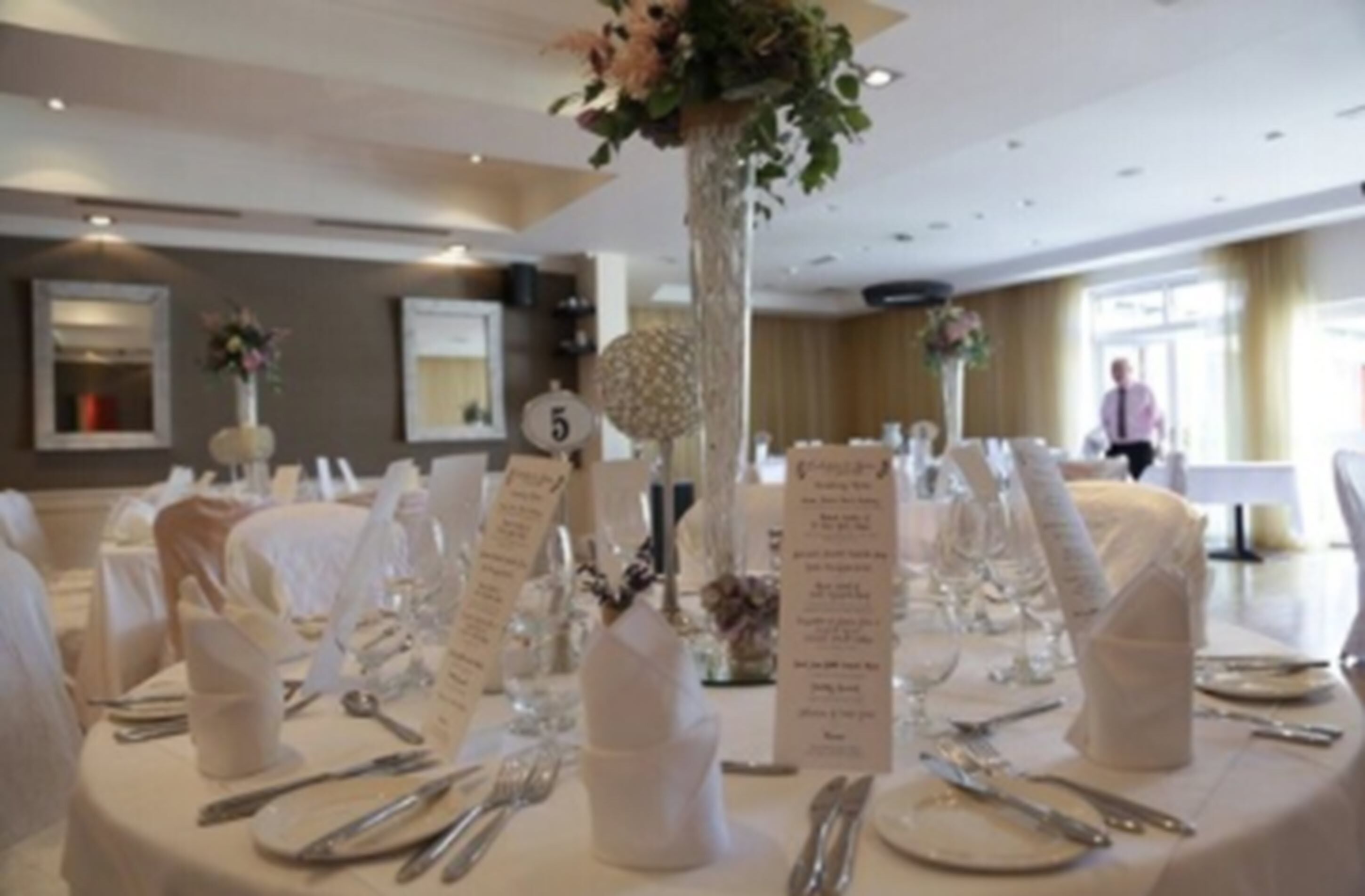 A banquet hall with round tables set for a formal event, numbered signs, and floral centerpieces.