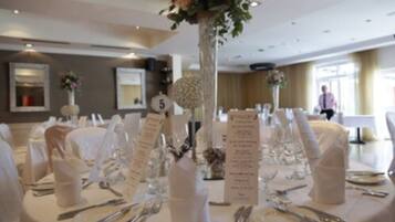 A banquet hall with round tables set for a formal event, numbered signs, and floral centerpieces.