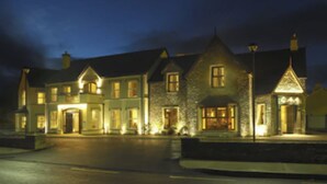 A large, multi-story building with a stone facade and multiple windows, illuminated by warm lighting. - Brook Lane Hotel (Kenmare)