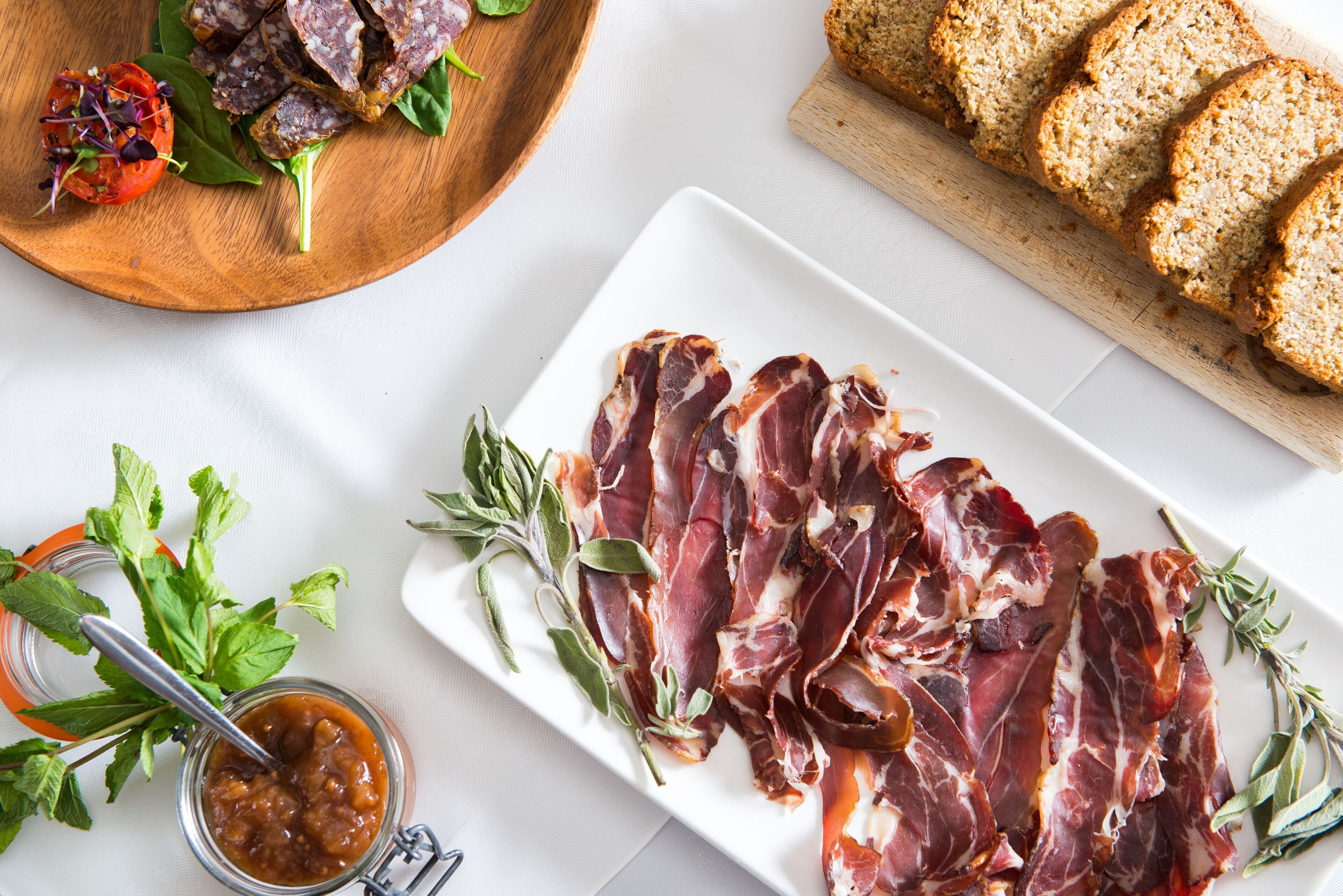 Une planche à découper en bois avec des tranches de viande, un pot de confiture et une assiette de pain.