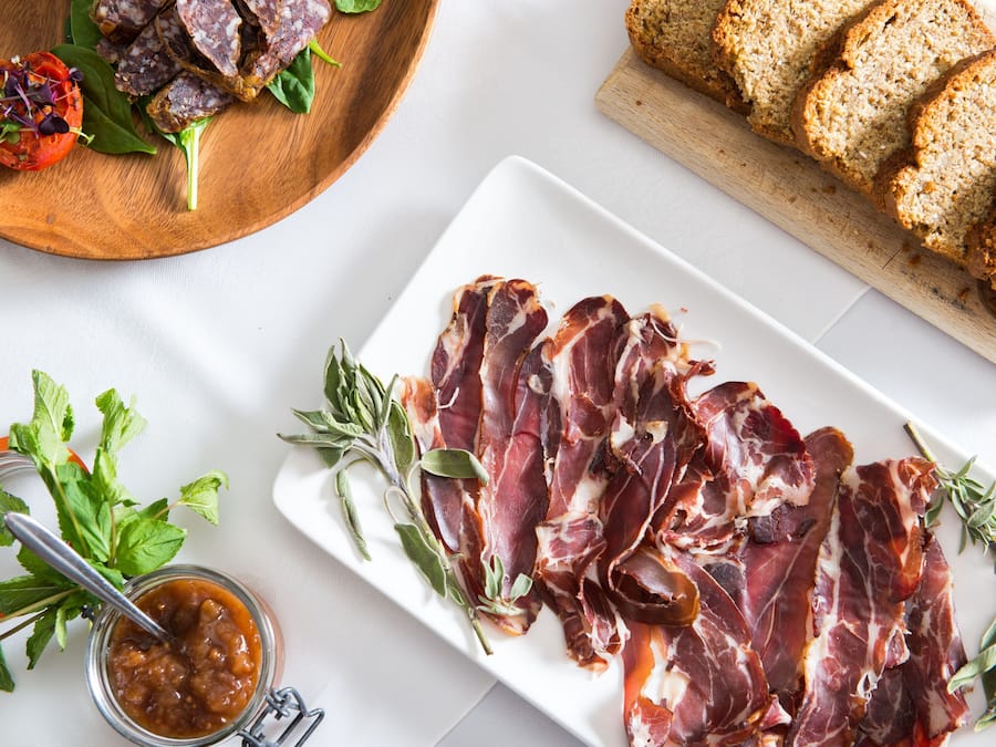 Une planche à découper en bois avec des tranches de viande, un pot de confiture et une assiette de pain.