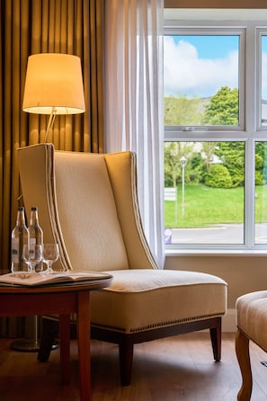 A hotel room with a large window, a chair, a table with a lamp, and a view of greenery outside. - Brook Lane Hotel (Kenmare)