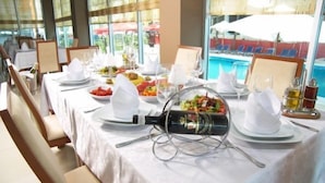 A dining table set for a meal with a bottle of wine, plates, glasses, and a fruit bowl. - AS Hotel (Golem)