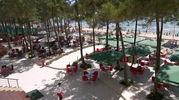 A beachside area with outdoor seating under umbrellas, a staircase leading to an upper level, and a view of the beach in the background. - AS Hotel (Golem)