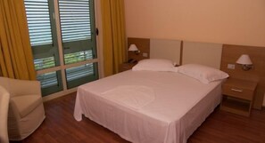 A hotel room with a bed, two bedside tables with lamps, a chair, and a window with blinds.