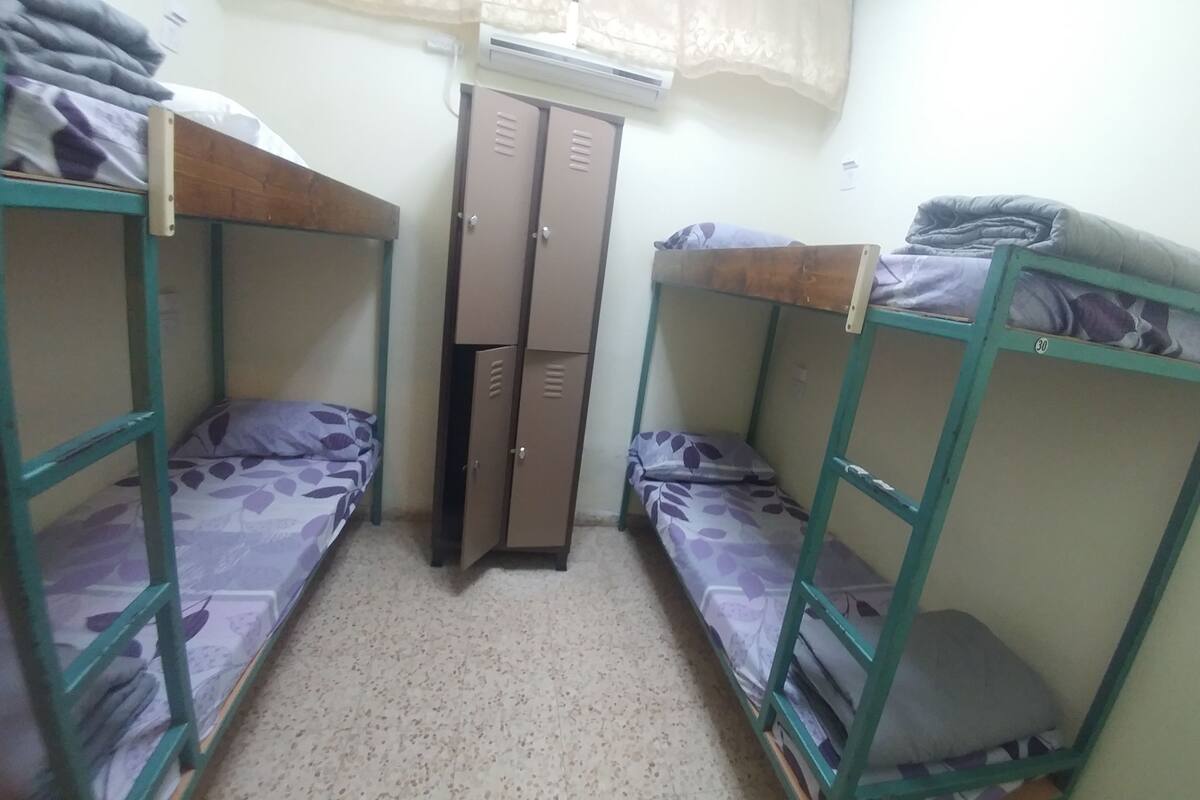 A dormitory room with bunk beds, a wardrobe, and a small window.