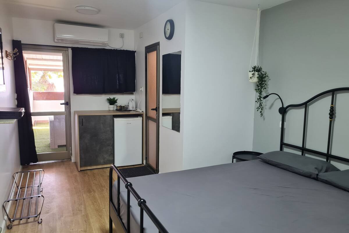 A compact room with a bed, a small kitchenette, a door leading to an outdoor area, and a ceiling fan.