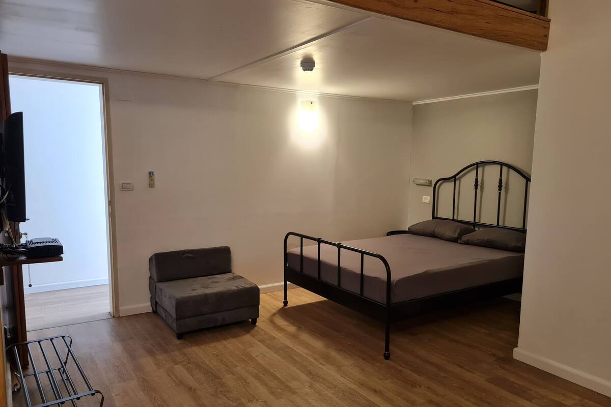 A bedroom with a bed, a small sofa, a TV, and a wooden floor.