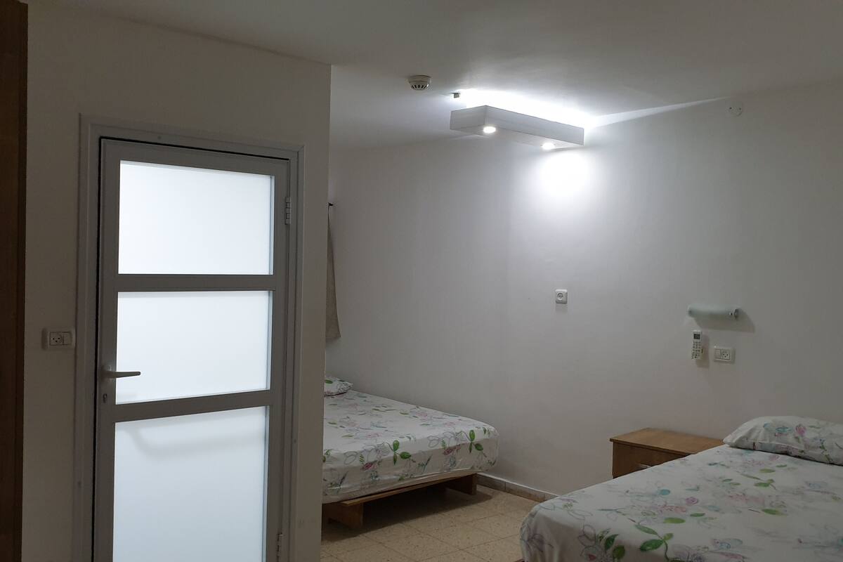 A bedroom with two single beds, a ceiling light, a wall-mounted thermostat, and a door with frosted glass panels.