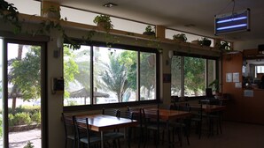 A restaurant with large windows, wooden tables, and chairs. - Arava Hostel (Eilat)