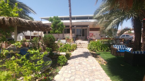 A courtyard with a stone pathway, outdoor seating, and a building in the background. - Arava Hostel (Eilat)