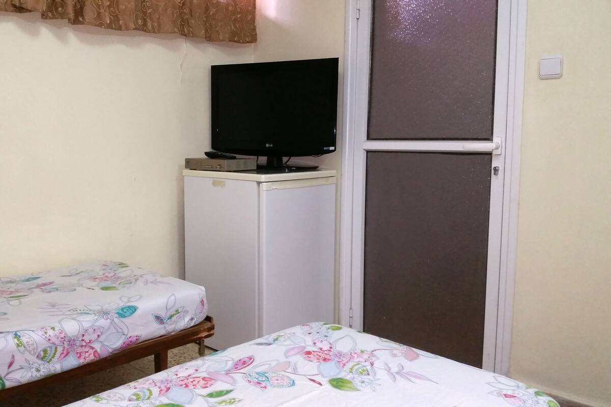 A small room with two beds, each with floral bedding, a television on a small cabinet, and a sliding door.