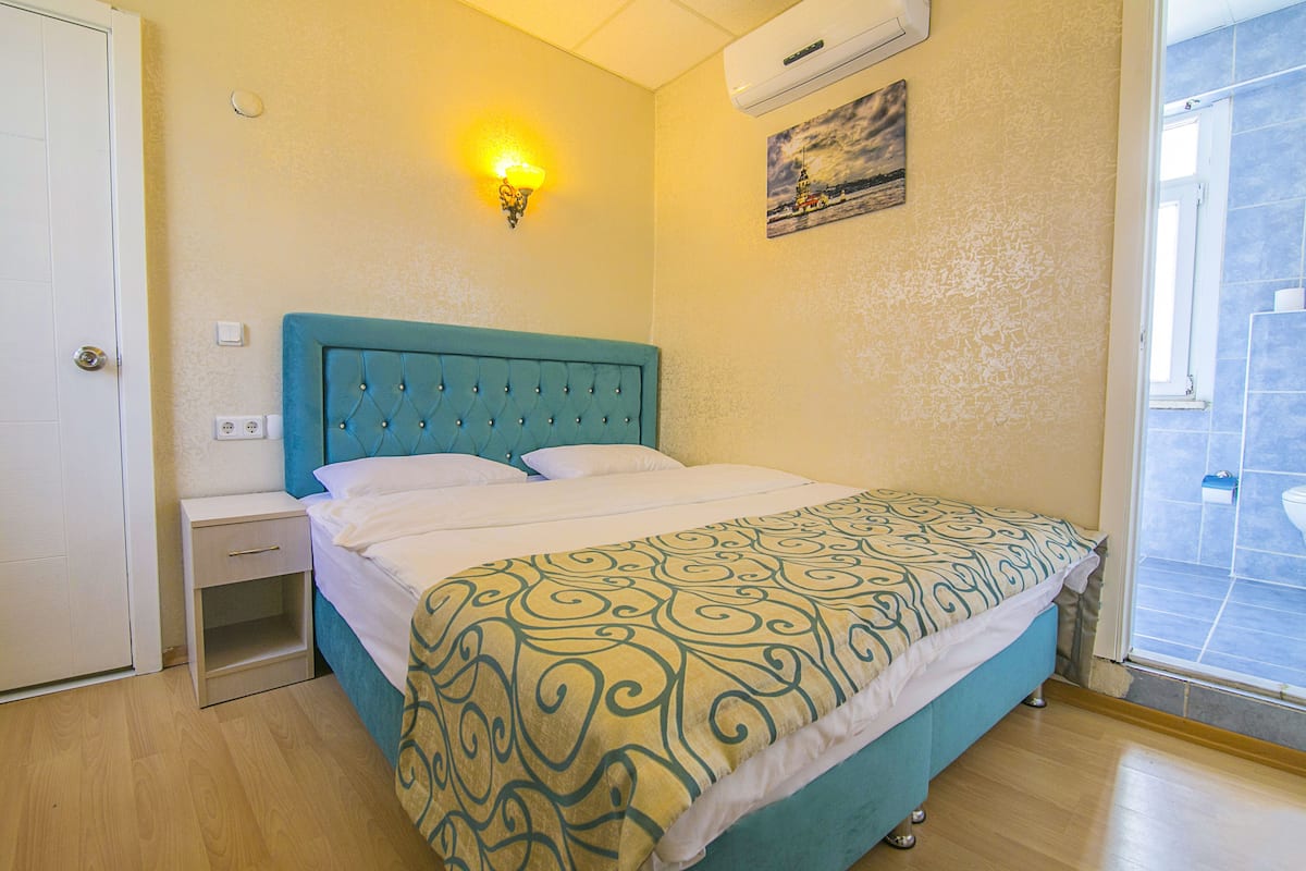 A bedroom with a bed, a nightstand, a wall-mounted light, and a window.