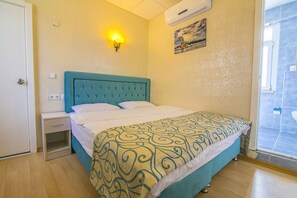 Un dormitorio con cama, mesita de noche, lámpara de pared y ventana.