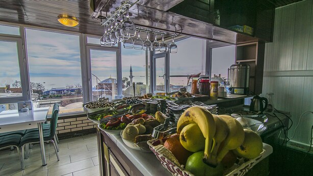 A buffet with a variety of fruits and vegetables, a coffee maker, and a view of a cityscape through large windows. - Ancient Town Hotel (Istanbul)