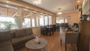 Een ruime woonkamer met een bank, een rond tafel en stoelen, grote ramen en een eethoek.