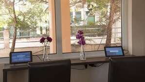 Een bureau met twee laptops en een vaas met paarse bloemen, geplaatst bij een raam met uitzicht op bomen en gebouwen.