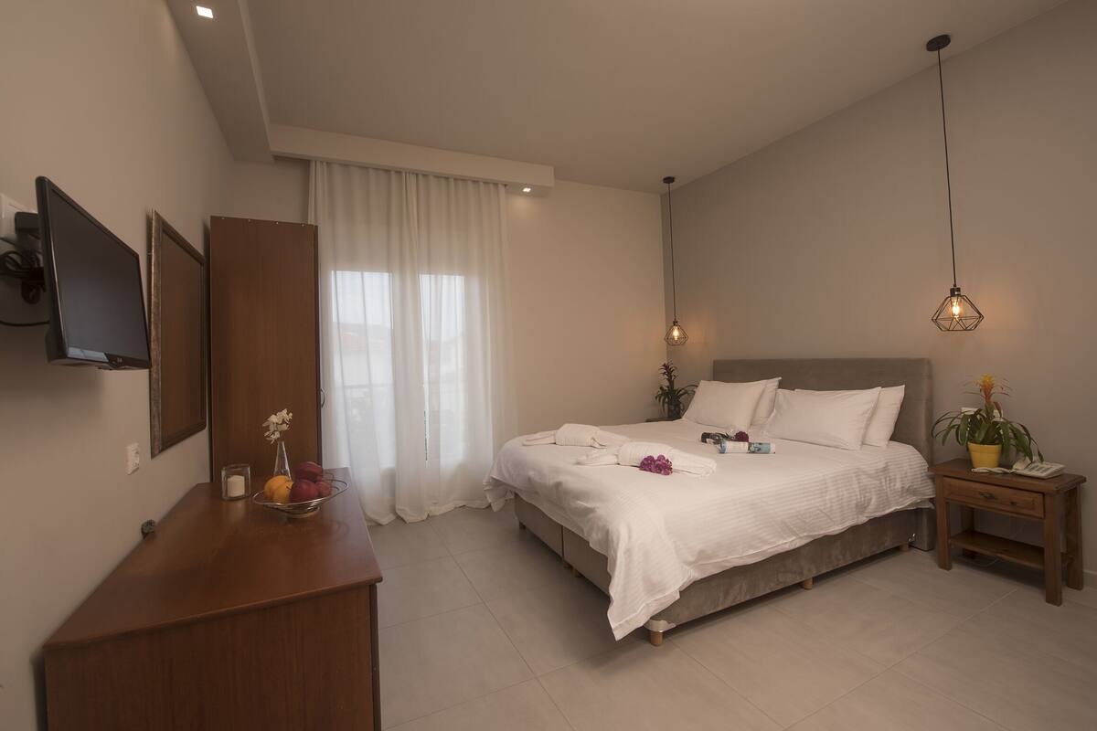 A modern bedroom with a large bed, bedside tables, a TV, and a window with curtains.
