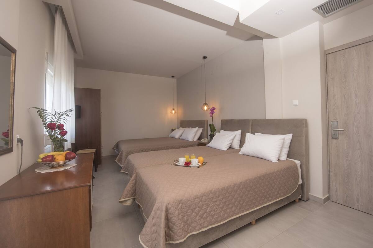 A hotel room with two beds, a wooden desk with a fruit bowl, and a mirror.