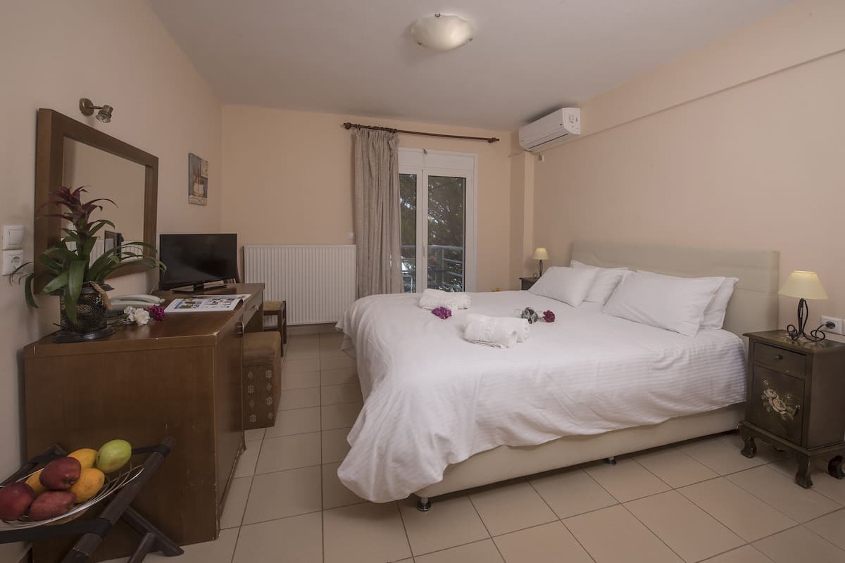 A hotel room with a bed, a desk with a computer, a mirror, a plant, and a fruit bowl.