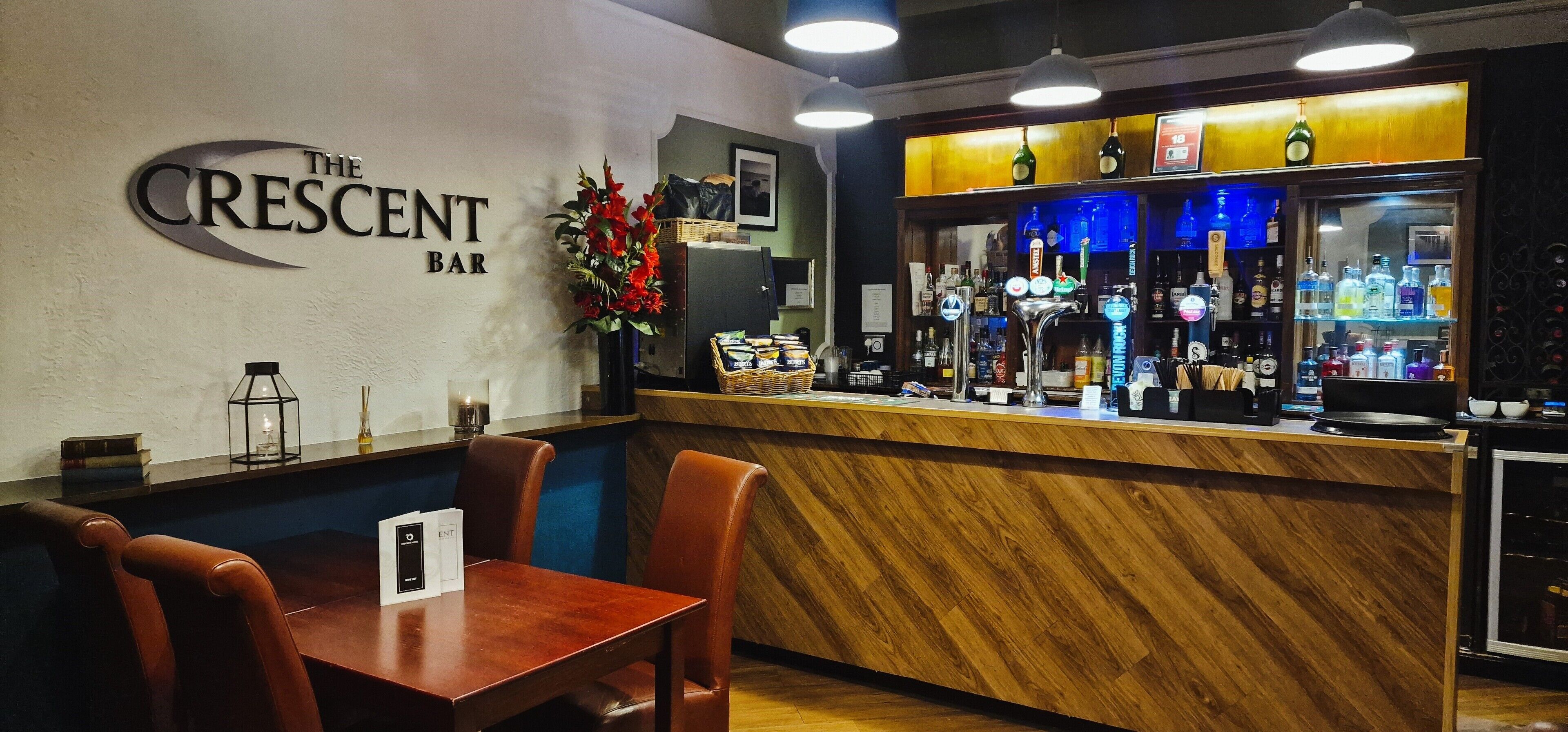 A bar area with a wooden counter, bar stools, and a menu stand.