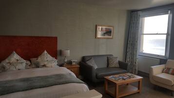 Una camera d'albergo con un letto, un divano grigio, un tavolino in legno, un comodino con una lampada e una finestra con tende.