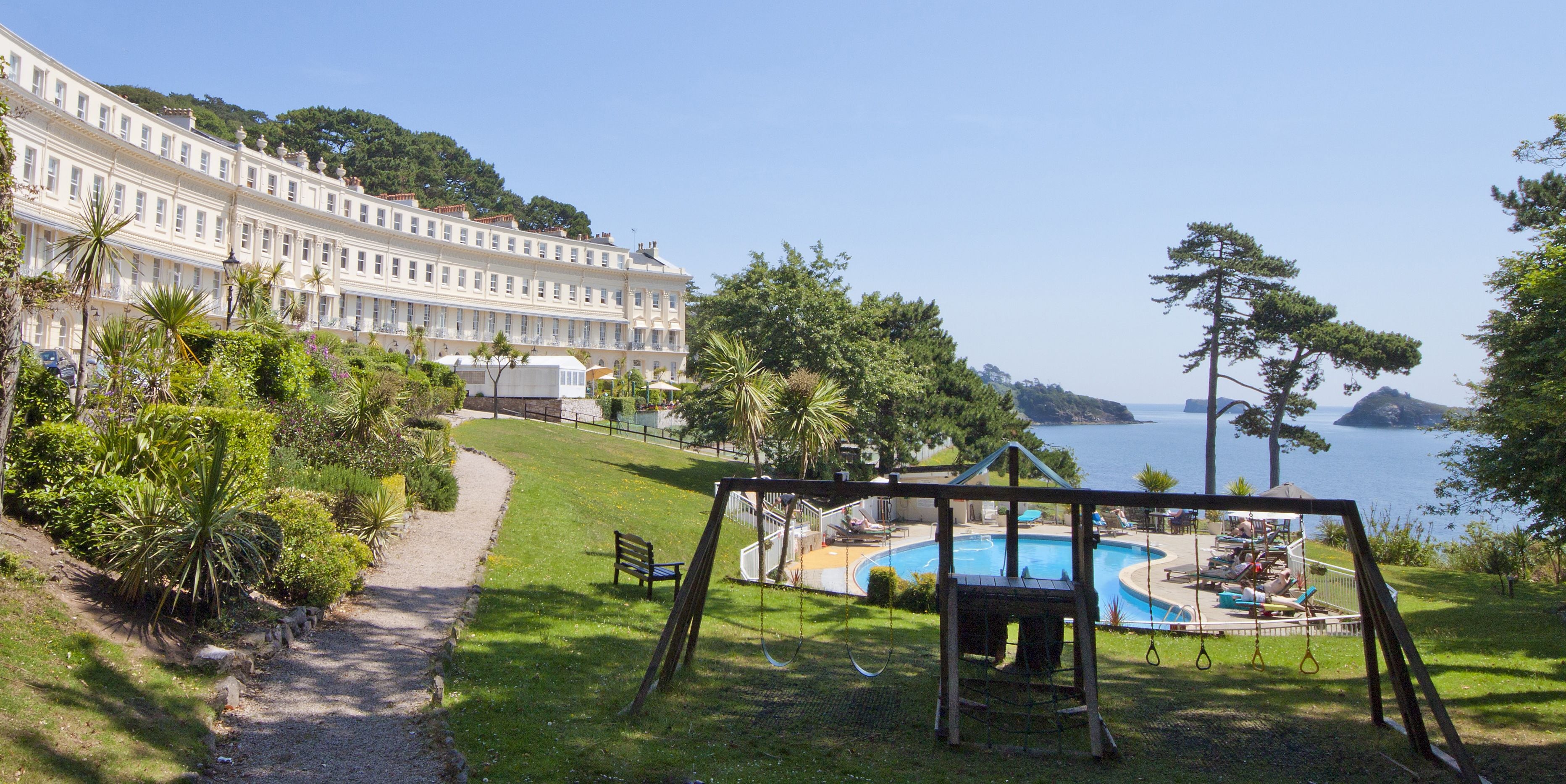 Un hotel con piscina, un conjunto de columpios y vista al mar.