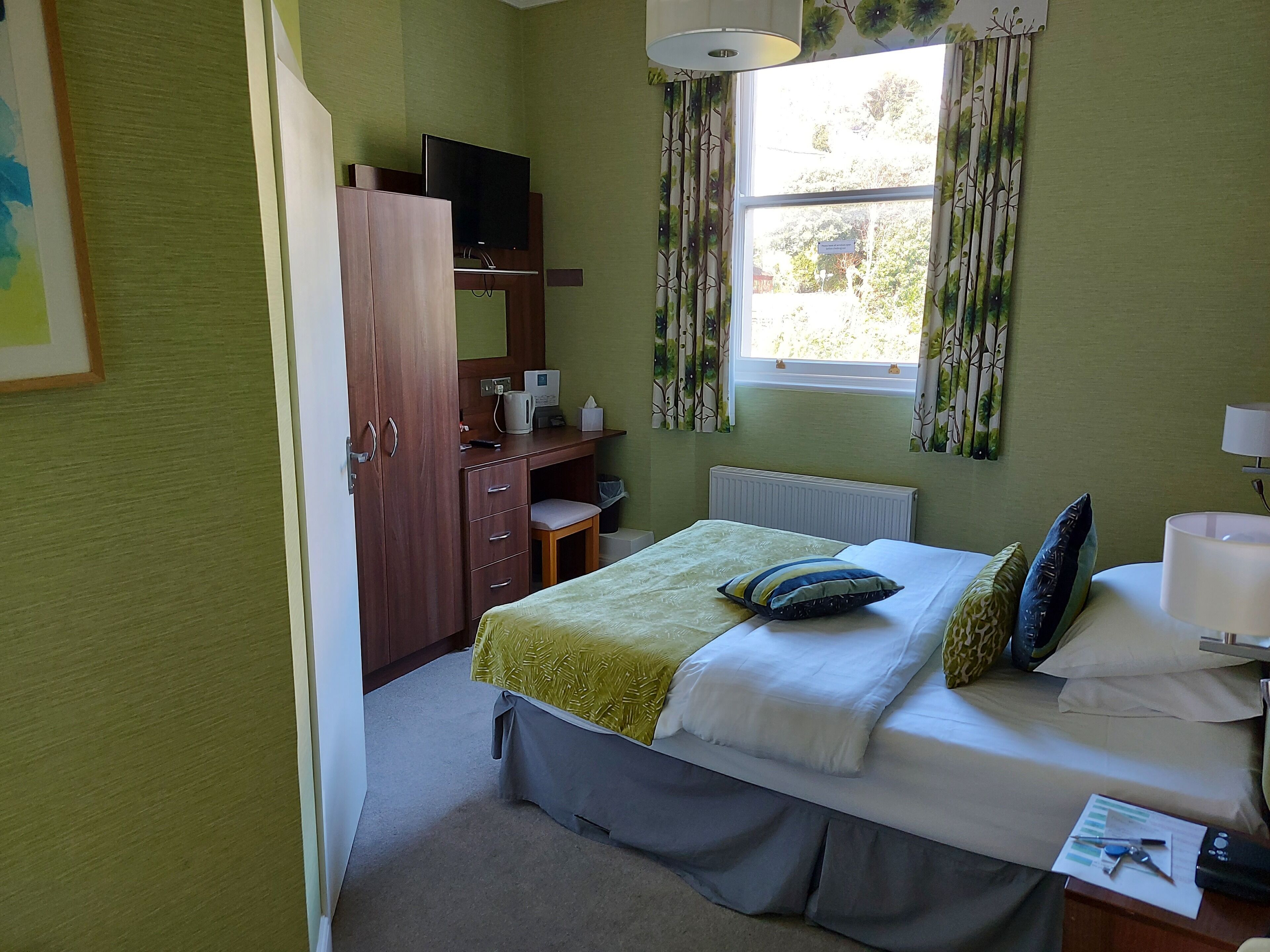 Ein Schlafzimmer mit einem Bett, einem Schreibtisch, einem Fernseher und einem Fenster mit Vorhängen.