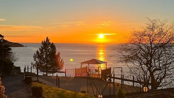 Ein Sonnenuntergangsblick von einem Balkon mit Blick auf ein Gewässer, im Vordergrund ein Gazebo und eine Steinmauer.