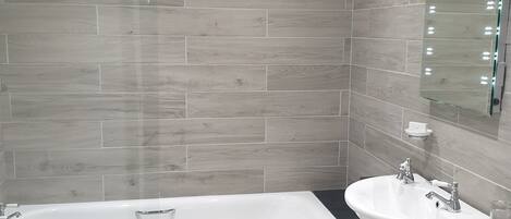 A modern bathroom with a bathtub, two sinks, and a large mirror.