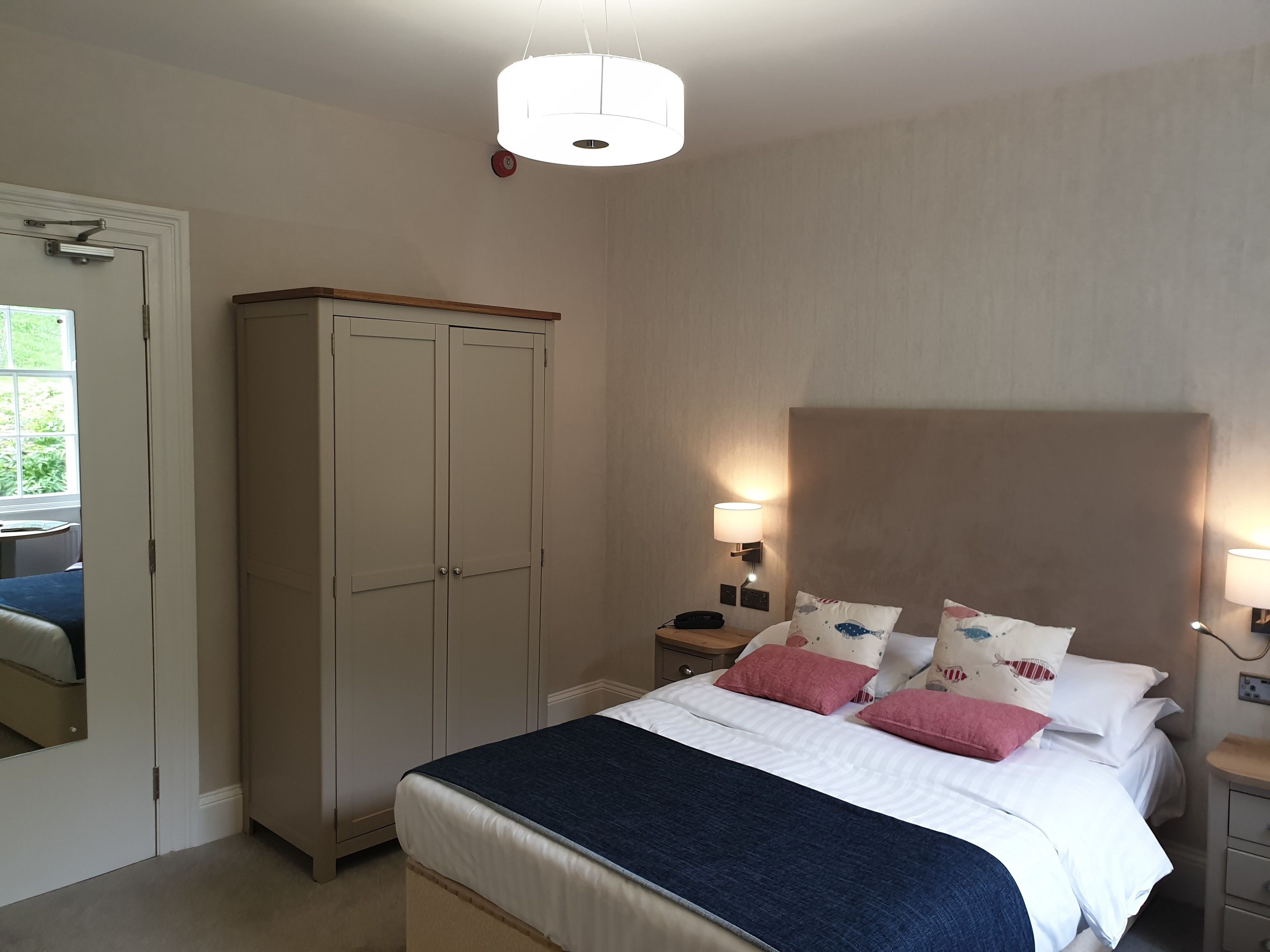 Une chambre à coucher comprenant un lit, des tables de chevet, une armoire et un luminaire suspendu.