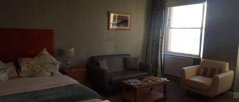 Una habitación de hotel con una cama, un sofá, una silla, una mesita y una ventana con cortinas.