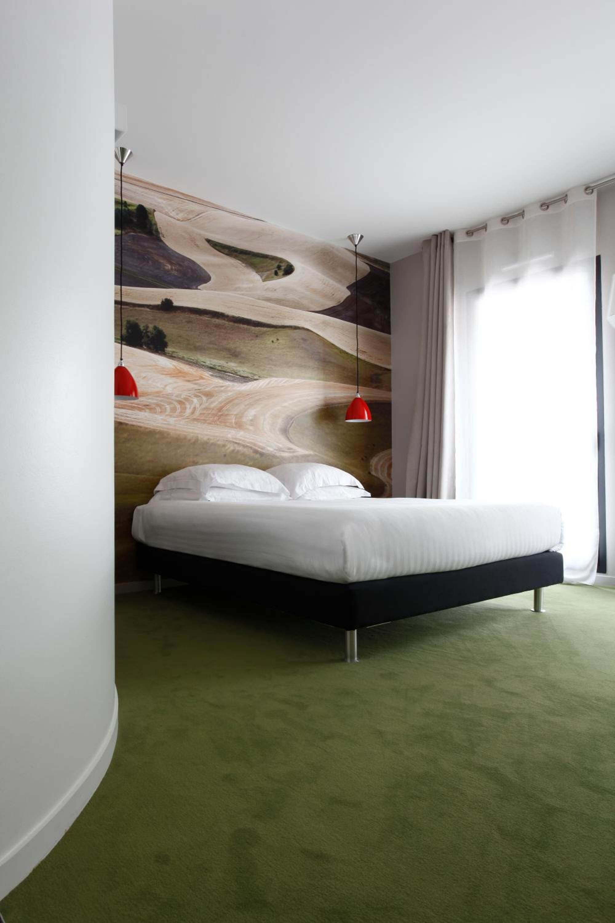 Une chambre à coucher avec un lit, une moquette verte, une fresque murale et des lampes suspendues rouges.