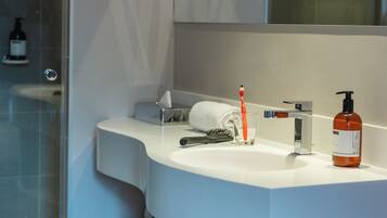 A modern bathroom with a white sink, a mirror, a towel, a toothbrush, a bottle of liquid soap, and a bottle of shampoo.