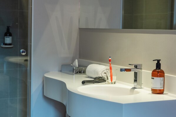 A modern bathroom with a white sink, a mirror, a towel, a toothbrush, a bottle of liquid soap, and a bottle of shampoo. - Hôtel L'échappée Belle (L'Isle-Jourdain)