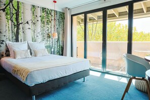 Un dormitorio moderno con una cama grande, vistas al exterior a través de un ventanal corredero y una pequeña mesa con una silla.