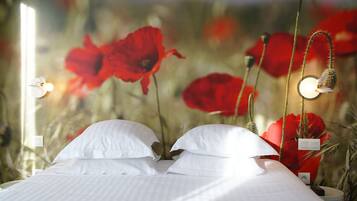 A bed with white linens and pillows, a bedside table with a lamp, and a wall with a poppy flower mural.