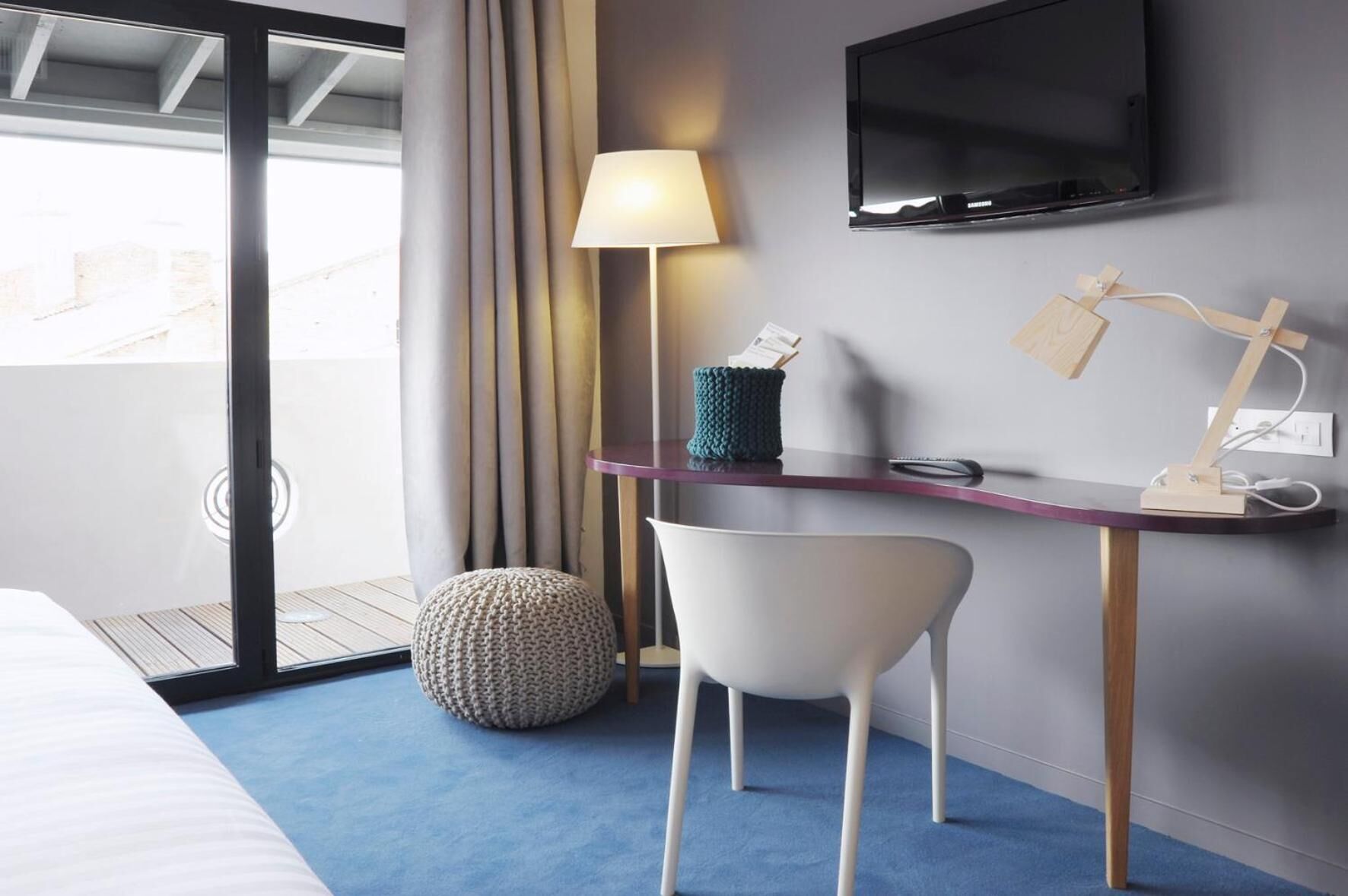 Una habitación de hotel moderna con cama, escritorio con lámpara, televisión y vistas al exterior.