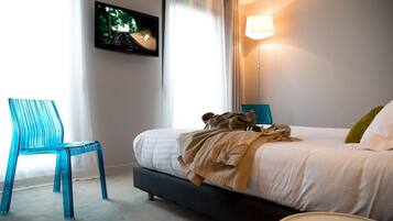 A hotel room with a bed, a TV mounted on the wall, a chair, and a bedside lamp.
