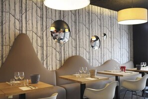 Interior de restaurante con diseño moderno, que presenta una pared de mármol con motivos de árboles, espejos redondos y mobiliario contemporáneo.