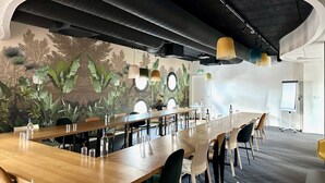 Ein Konferenzraum mit einem langen Tisch, Stühlen, einer Tafel und einem Wandgemälde von tropischen Pflanzen.